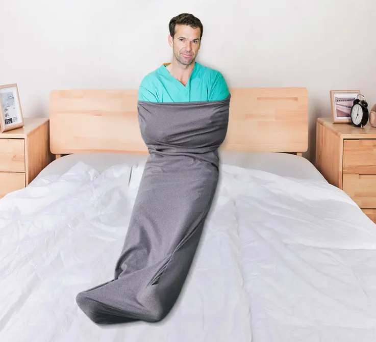 Person wrapped in a gray mermaid tail blanket on a bed.